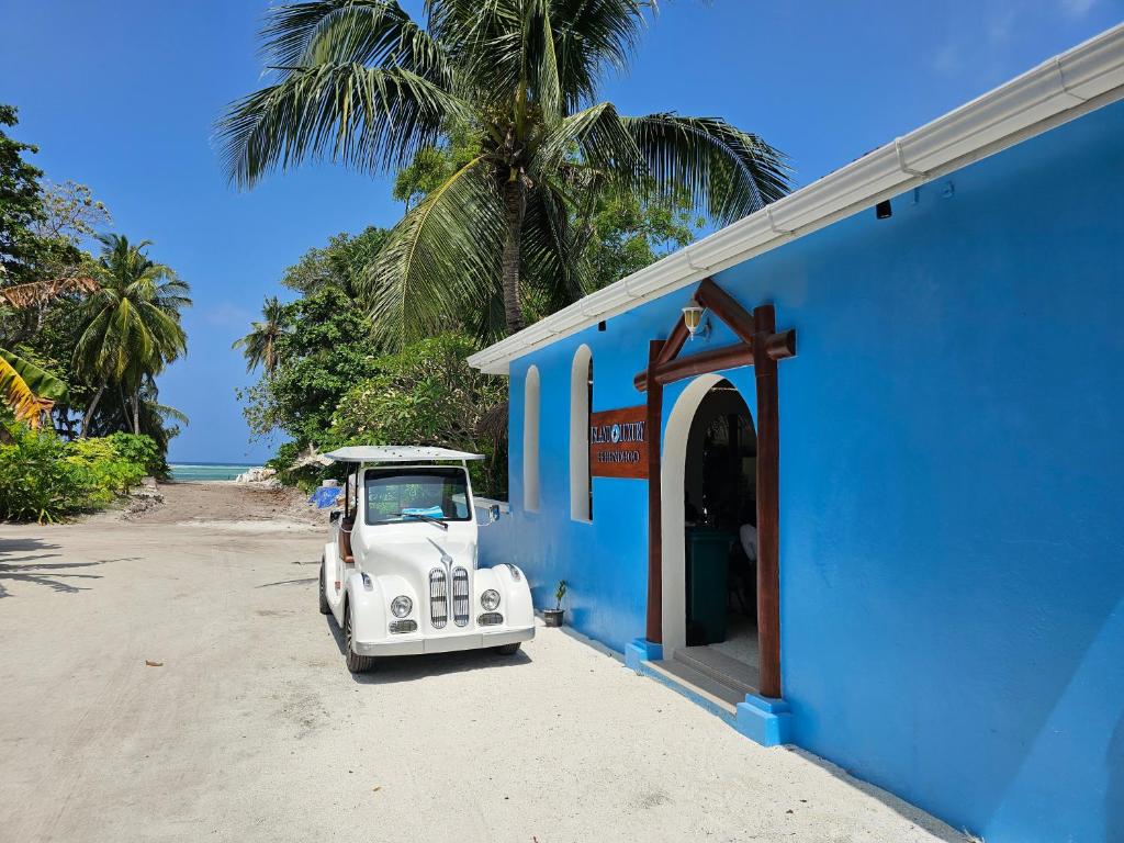 un viejo coche blanco aparcado fuera de un edificio azul en Island Luxury Fehendhoo en Fehendhoo