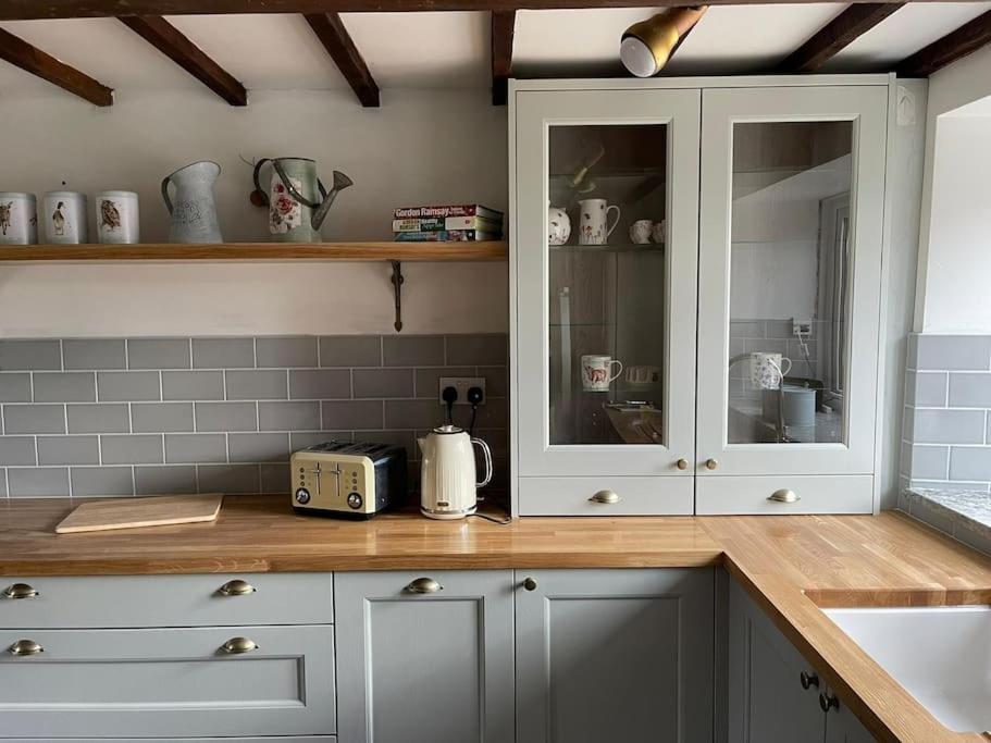 cocina con armarios blancos y encimera en Gardeners Cottage near the Norfolk Coast, en Knapton
