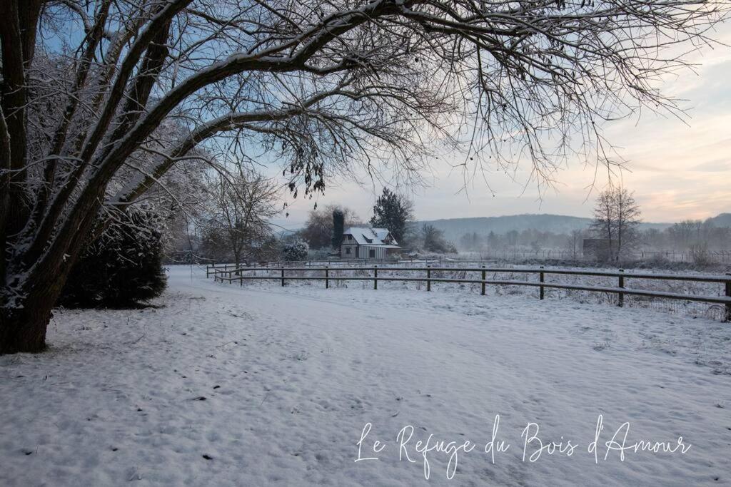 a snow covered field with a fence and a house at Le Refuge du Bois d'Amour in Arnières-sur-Iton