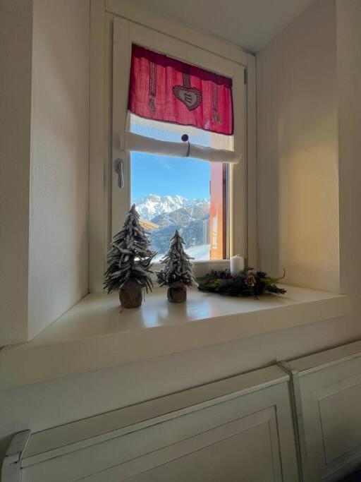 a window with two christmas trees on a window sill at Trilocale con vista piste da sci in Villa Dalegno