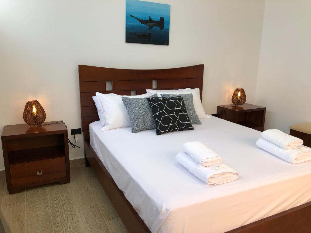 1 dormitorio con 1 cama blanca grande y 2 mesitas de noche en Suites en el paraíso San Cristóbal Galápagos, en Puerto Baquerizo Moreno