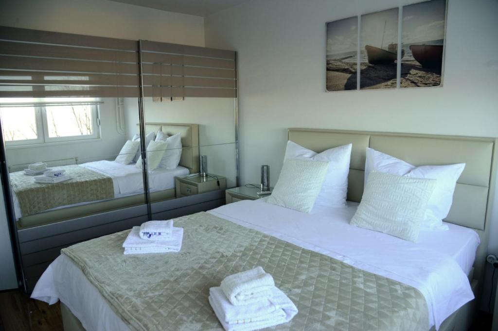 um quarto com 2 camas com lençóis brancos e espelhos em Irina Lux Apartment em Negotin
