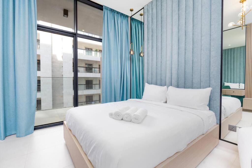 een slaapkamer met een groot wit bed en blauwe gordijnen bij Studio - 3min from Metro station - Westwood by Imtiaz in Dubai