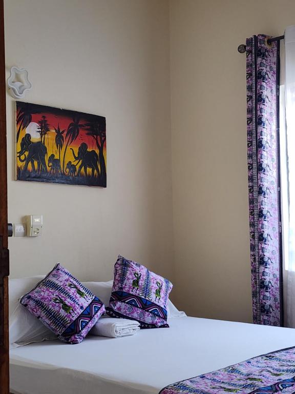 a bed with purple pillows and a painting on the wall at Home away from Home in Cococodji