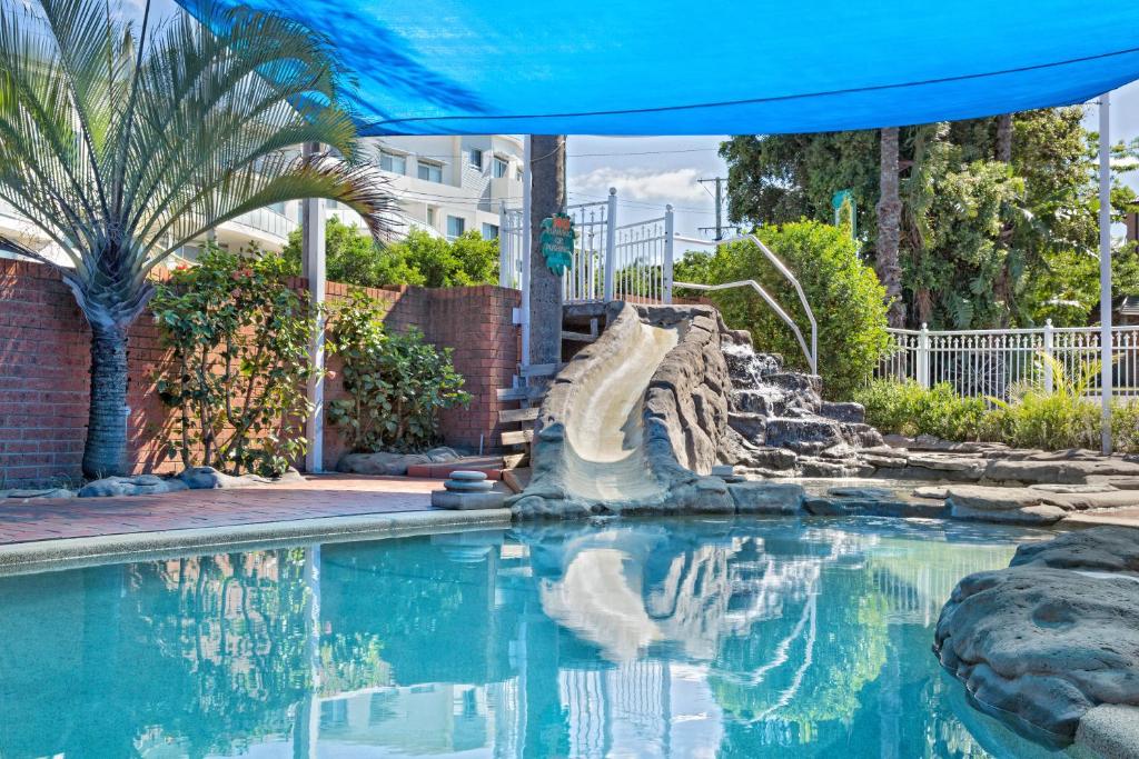 een zwembad met een blauwe parasol en een waterglijbaan bij Sapphire Palms Motel in The Entrance