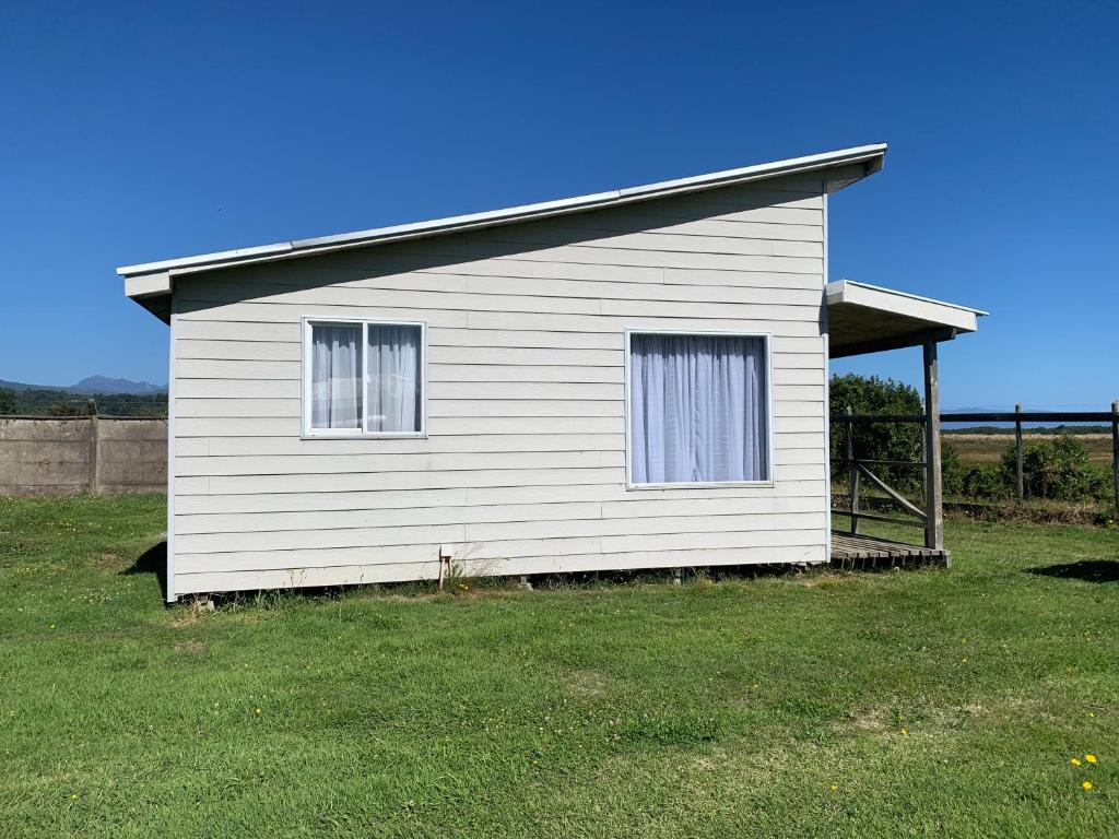 ein weißes Haus mit zwei Fenstern auf einem Feld in der Unterkunft Cabaña Raihuè Austral in Puerto Montt