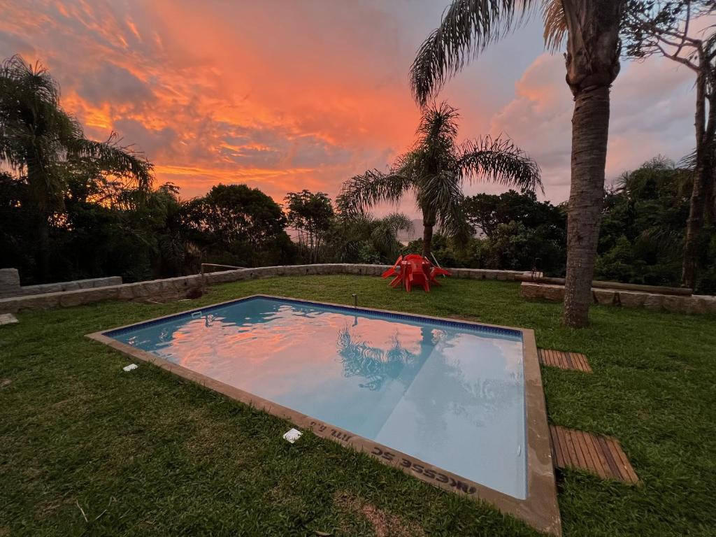 una piscina en el césped con una puesta de sol en el fondo en Natural Forest en Praia do Rosa