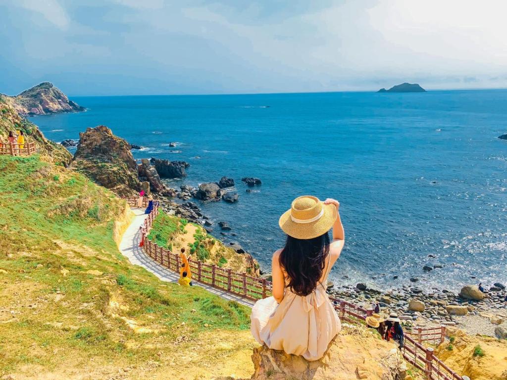 uma mulher sentada num penhasco a olhar para o oceano em Hòa Lợi Hotel em Quy Nhon