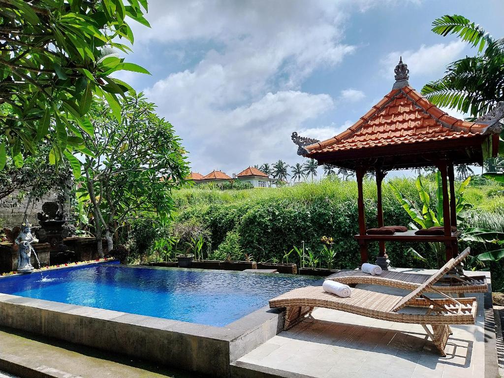 - une piscine avec un kiosque et un banc à côté d'une piscine dans l'établissement Puri Prana Guest House, à Ubud