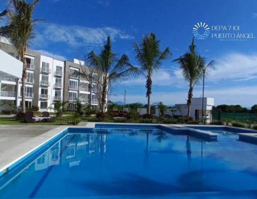 a pool with palm trees in front of a building at Encanto de Depa c/ Alberca y Club de Playa Privado in Barra Vieja