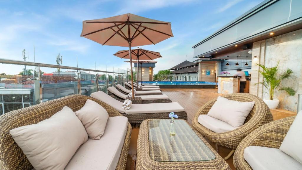 een patio met rieten stoelen en tafels en een parasol bij City of Aventus Hotel - Denpasar in Denpasar