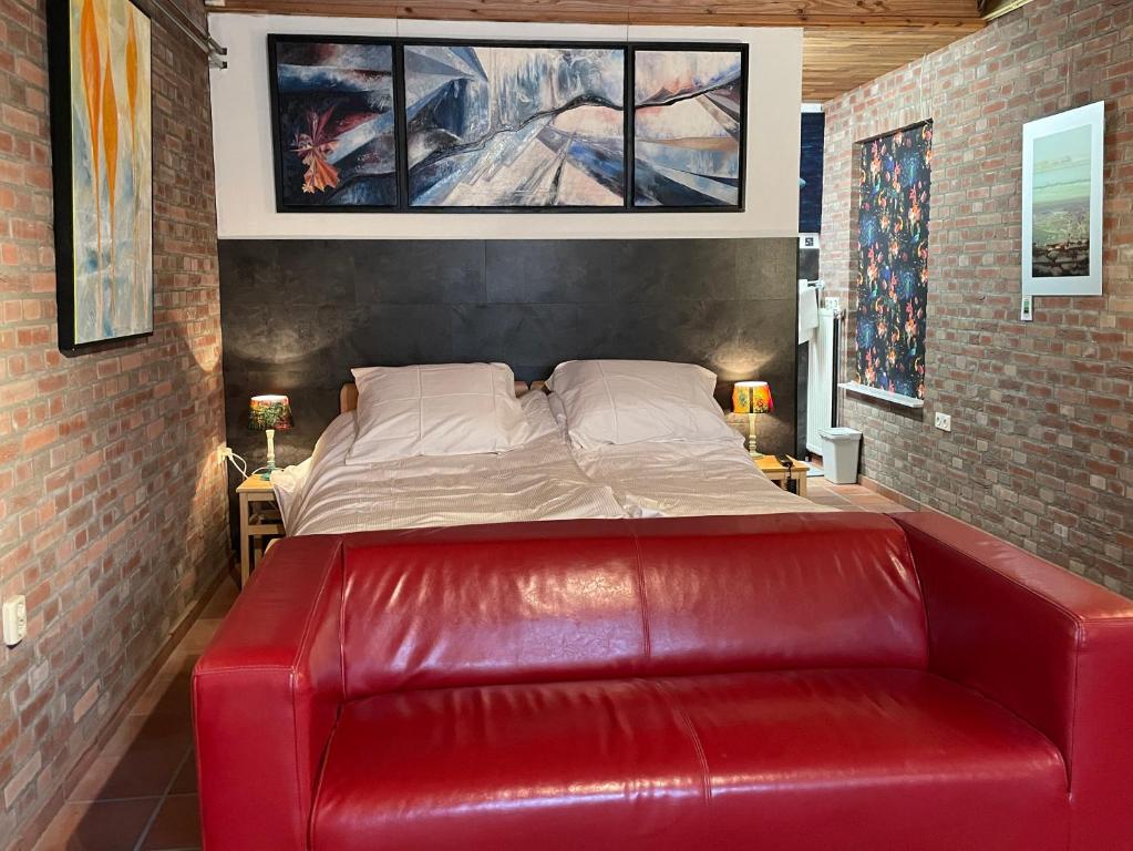 a red leather couch in a room with a bed at 't ouw ateljeeke in Budel