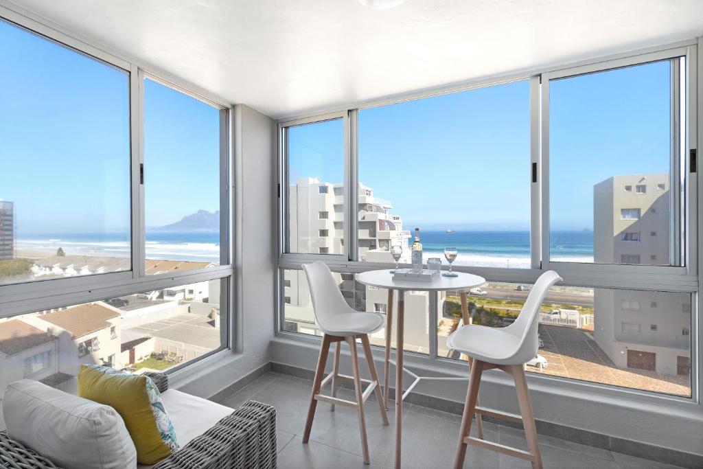 a living room with a table and chairs in front of windows at Ocean View 503 in Bloubergstrand