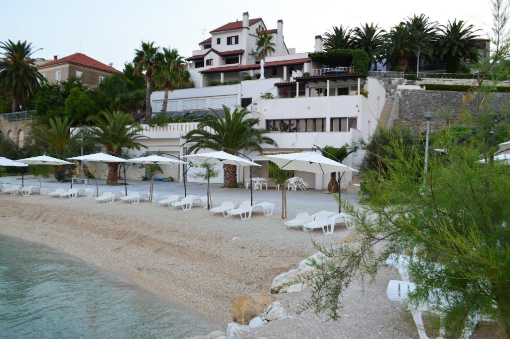 a beach with white chairs and umbrellas and a building at Beach Villa Bozikovic in Podstrana