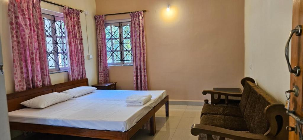 a bedroom with a bed and a chair and two windows at SERENE VIBE MAJORDA in Goa