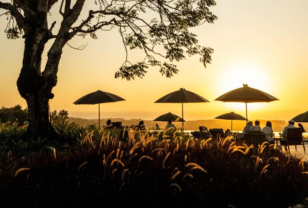 a group of people sitting under umbrellas at sunset at Grün Resort Uluwatu in Uluwatu