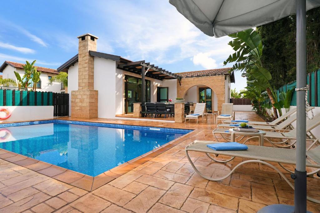 uma piscina com cadeiras e um guarda-sol ao lado de uma casa em Villa Anthia - 2bed with Large Pool em Agia Napa