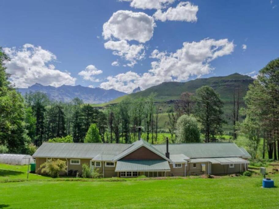 una casa grande con un campo verde y montañas en Ondini Cottage, en Drakensberg Garden