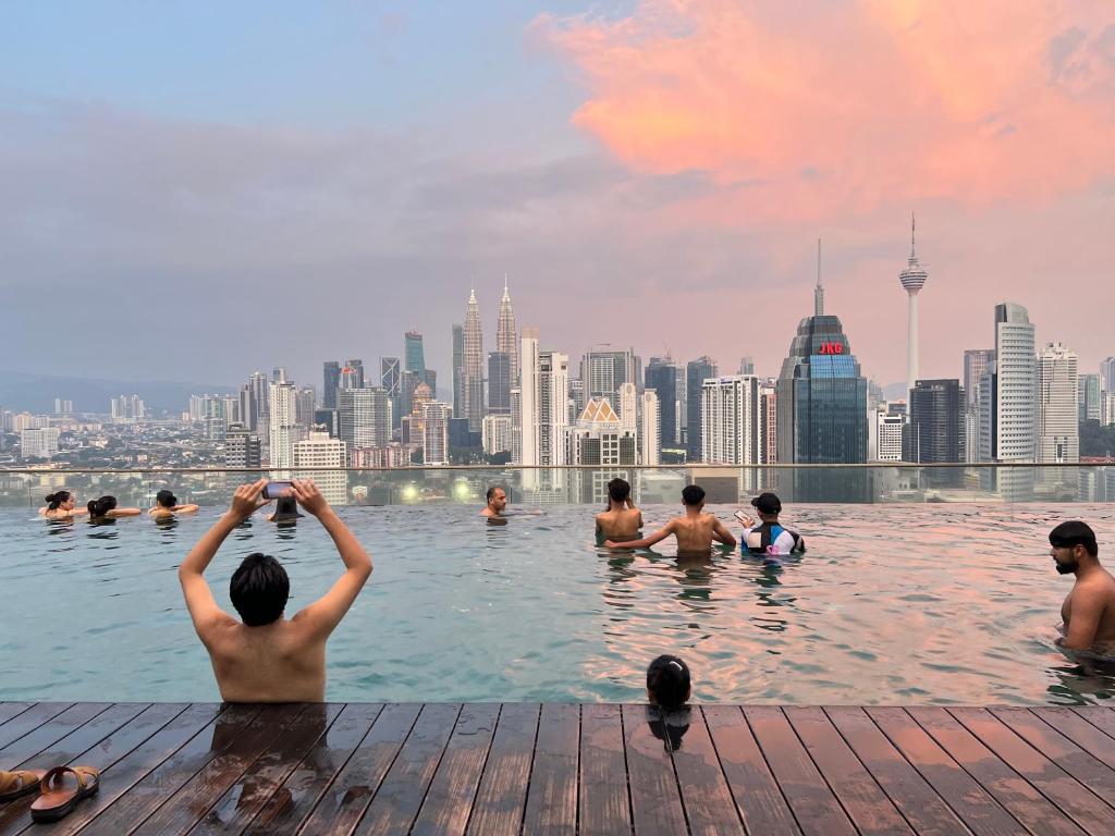 a group of people swimming in a pool with a city skyline at Empire Hostel Regalia in Kuala Lumpur