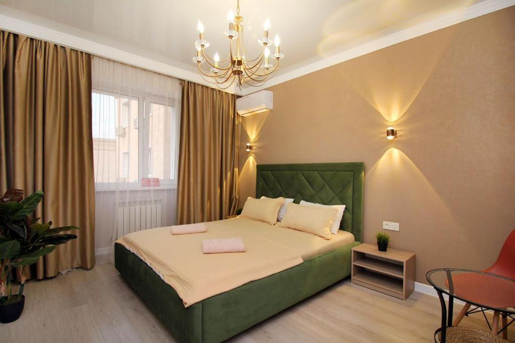 ein Schlafzimmer mit einem grünen Bett und einem Kronleuchter in der Unterkunft Апартаменты в центре Алматы in Almaty