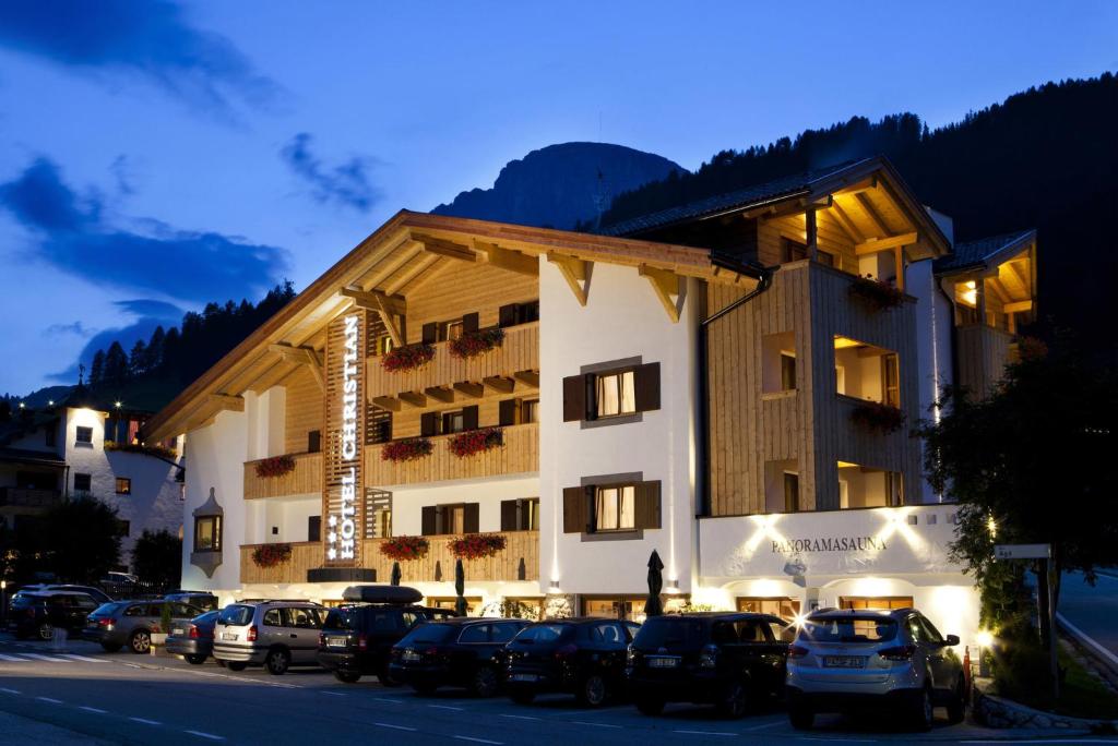 un grand bâtiment avec des voitures garées devant lui dans l'établissement Hotel Christian, à Corvara in Badia