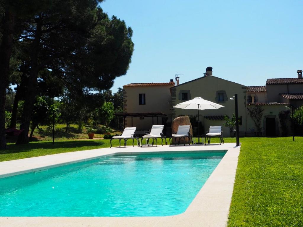 a pool with chairs and an umbrella next to a house at Masia Can Pitu in Santa Cristina d'Aro