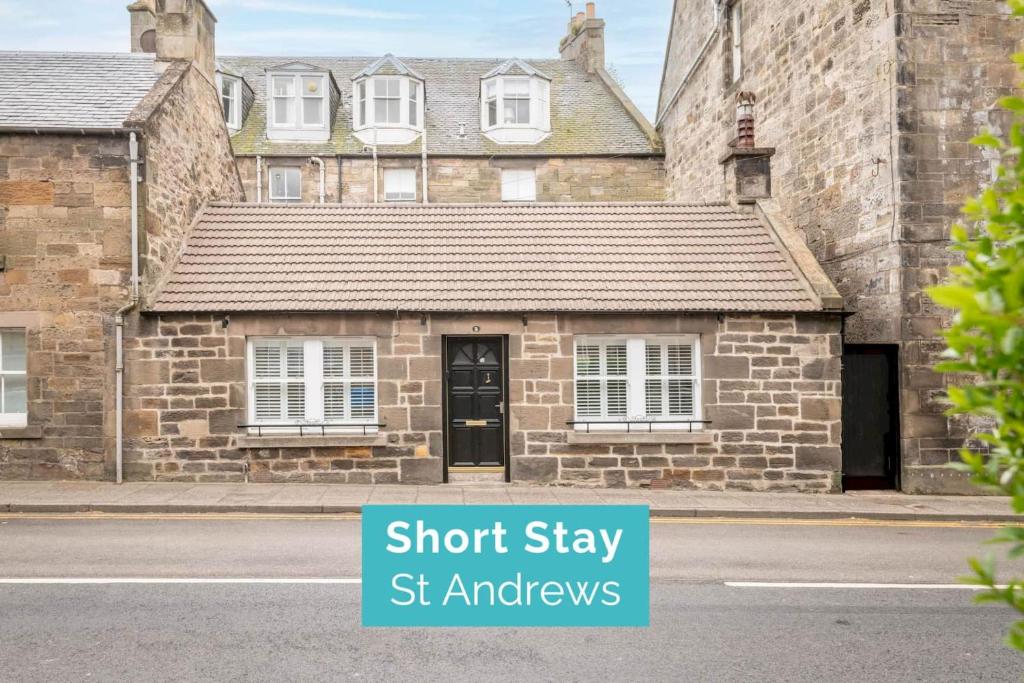 ein altes Backsteinhaus mit einem Schild, auf dem steht: Kurzaufenthalt Botschafter in der Unterkunft The Golf Cottage - 30 Seconds to The Old Course in St Andrews