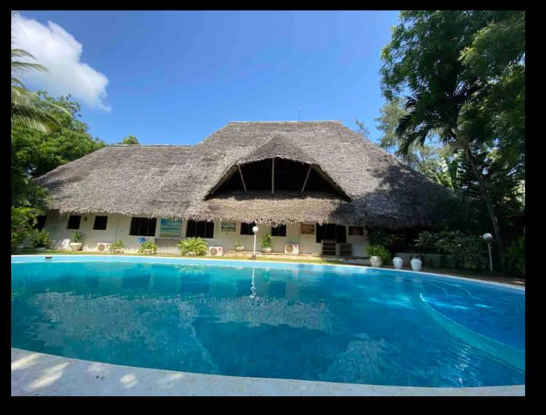 een gebouw met een rieten dak en een zwembad bij Ornella House Resort: Spacious 5-Bed Villa in Tropical Malindi in Malindi