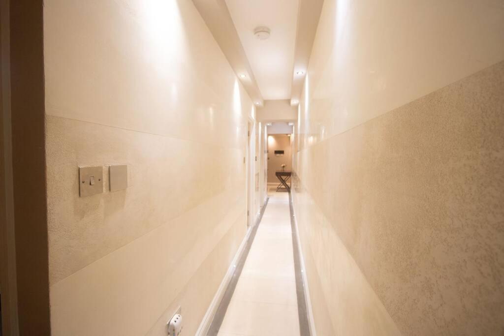 un pasillo con un largo pasillo con paredes blancas en OikosHomes Three Bedroom Flat in London, en Londres