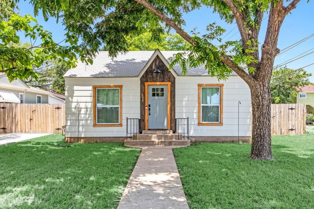 a white house with a tree in the yard at Bungalow Bliss - Large Backyard & Fire Pit in McGregor
