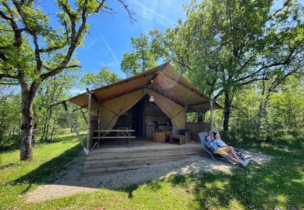 2 personnes assises dans une chaise devant une tente dans l'établissement Lodges du Bois Dodo - ancien Camping de Bois Redon, à Septfonds