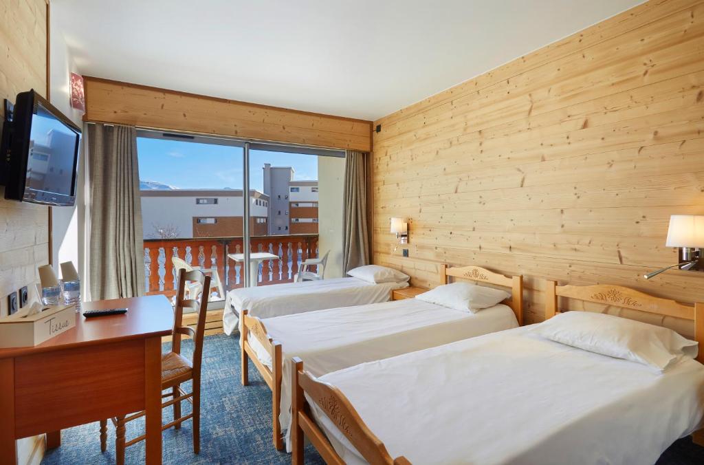 a hotel room with three beds and a desk and a television at Hôtel Eliova Le Chaix in L'Alpe-d'Huez