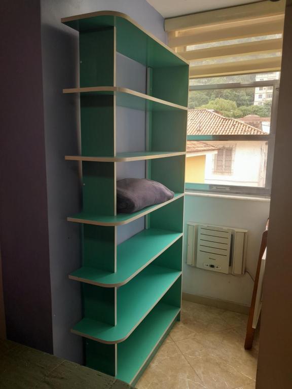 a green book shelf in a room with a window at Suíte confortavel in Rio de Janeiro