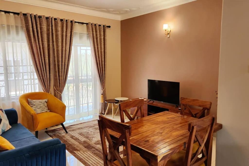 sala de estar con mesa de madera y TV en Sanz Cozy Stay; Butenga Estate, Kira. en Kira
