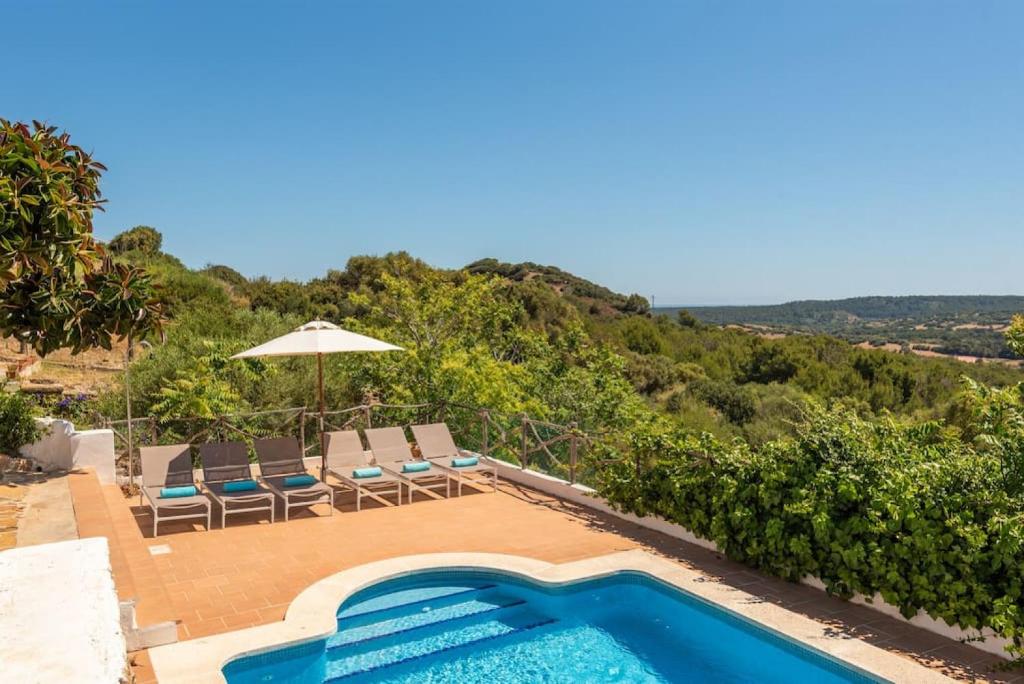 a swimming pool with chairs and an umbrella on a house at Finca BellaMirada in Es Mercadal