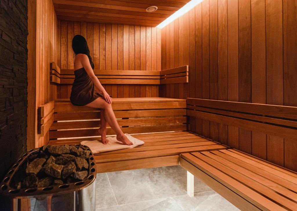 Woman wrapped in towel seated inside wooden sauna, warm lighting and relaxed posture