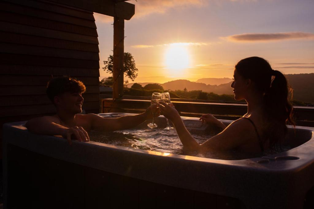 um homem e uma mulher sentados numa banheira de hidromassagem com um copo de vinho em Tan Y Bryn Glamping em Conwy