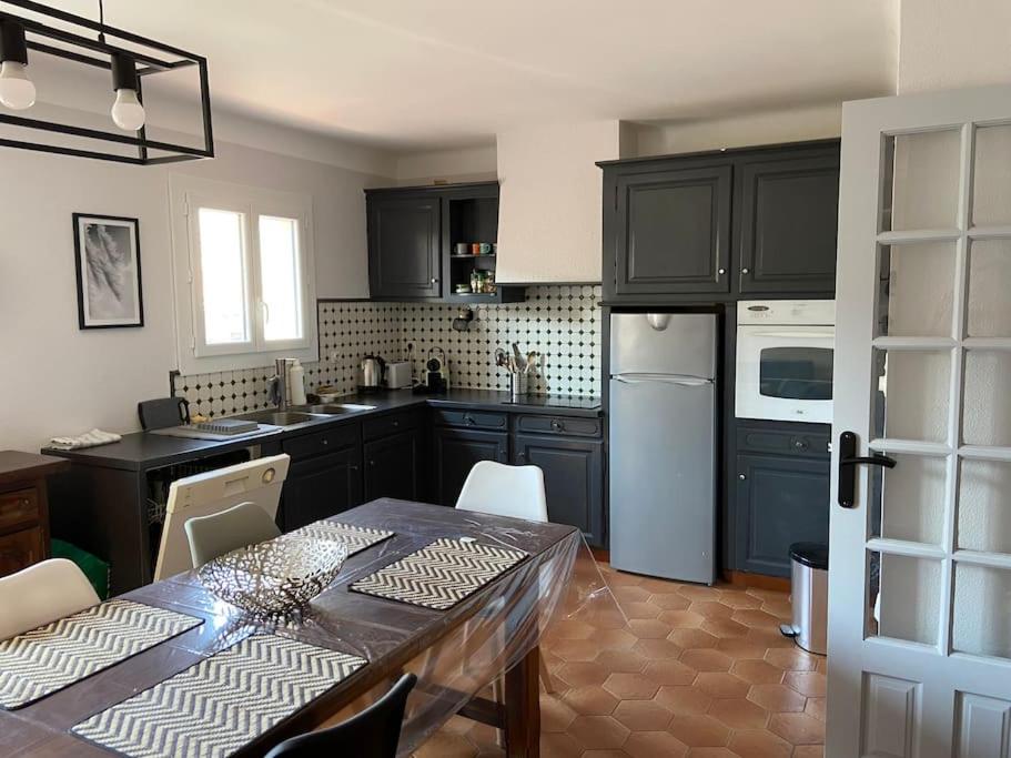 une cuisine avec des armoires noires et une table ainsi qu'une salle à manger dans l'établissement Grande maison familiale proche des plages, à Torreilles