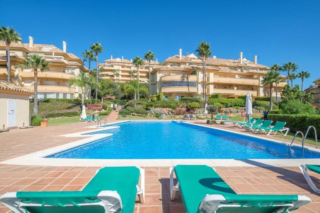 a swimming pool with green chairs and a building at R26 Stunning Penthouse Duplex Elviria in Marbella