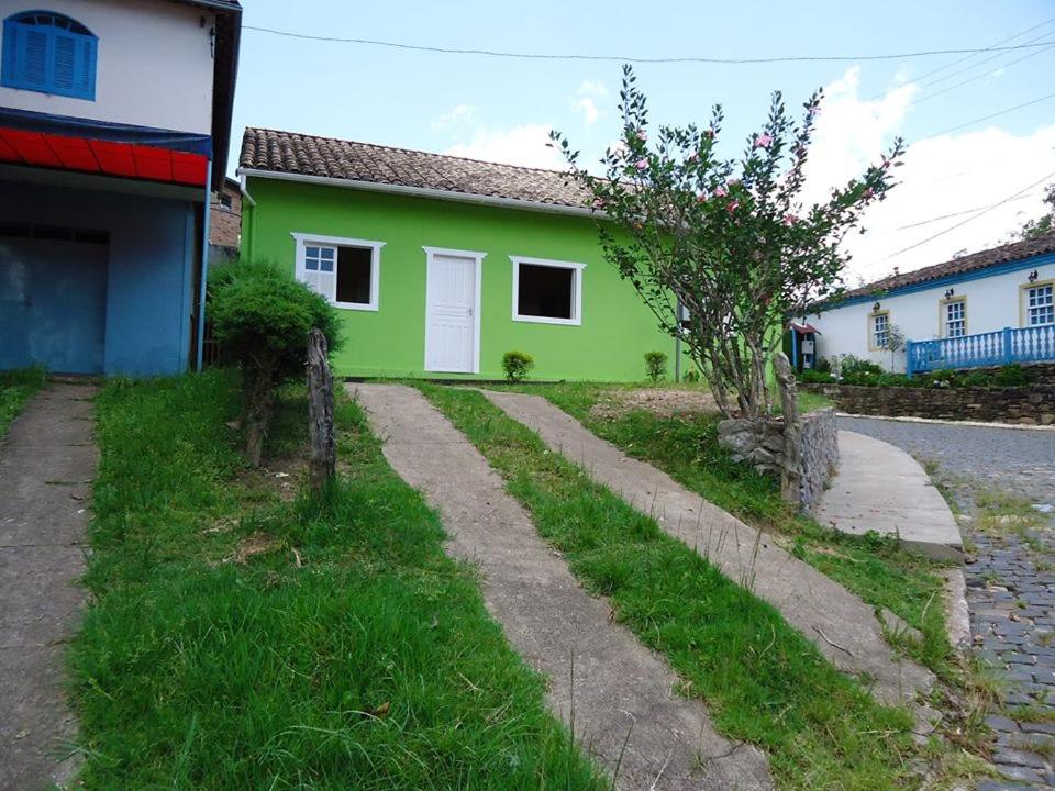 uma casa verde com uma árvore ao lado de uma rua em Casa no Centro de Ibitipoca em Lima Duarte