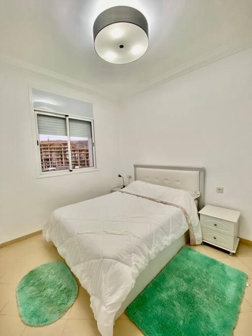 a white bedroom with a bed and two green rugs at Coquette studio 7 min plage in Agadir