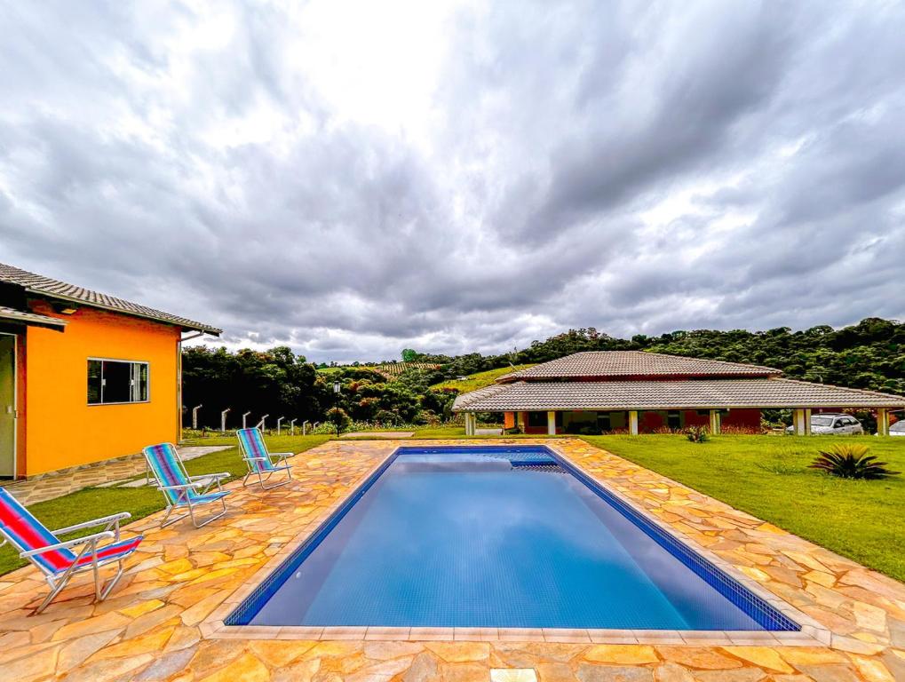 einen Pool mit zwei Stühlen und ein Haus in der Unterkunft Otima chacara c Wi-Fi e churrasq em Socorro SP in Socorro