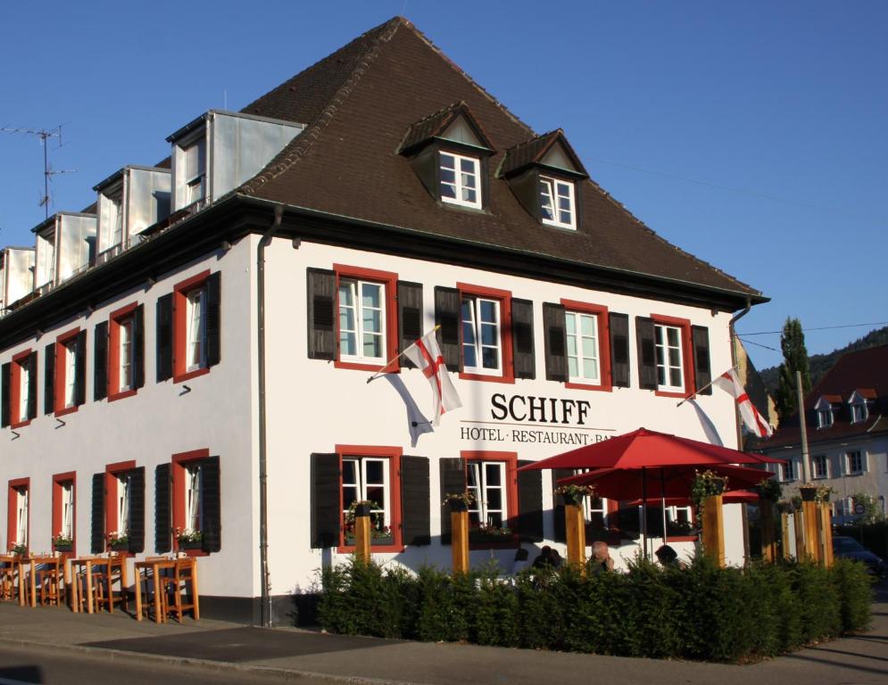 un grand bâtiment blanc avec volets rouges dans une rue dans l'établissement Gasthaus Schiff, à Fribourg-en-Brisgau