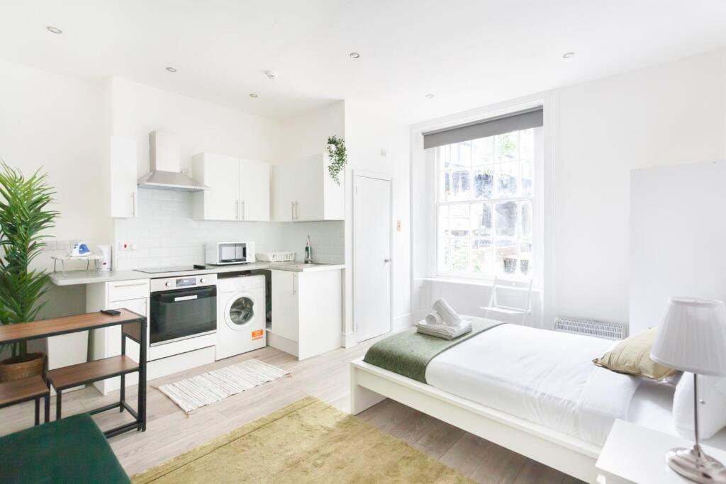 a white bedroom with a bed and a kitchen at Beautiful Studio Flat in Hackney next to Overground Station in London