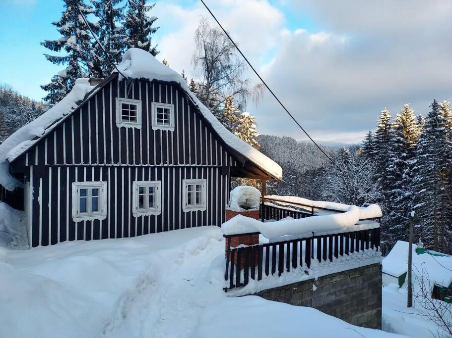 una casa bianca e nera con la neve sul tetto di Stylová roubená chalupa Jizerské hory a Kořenov