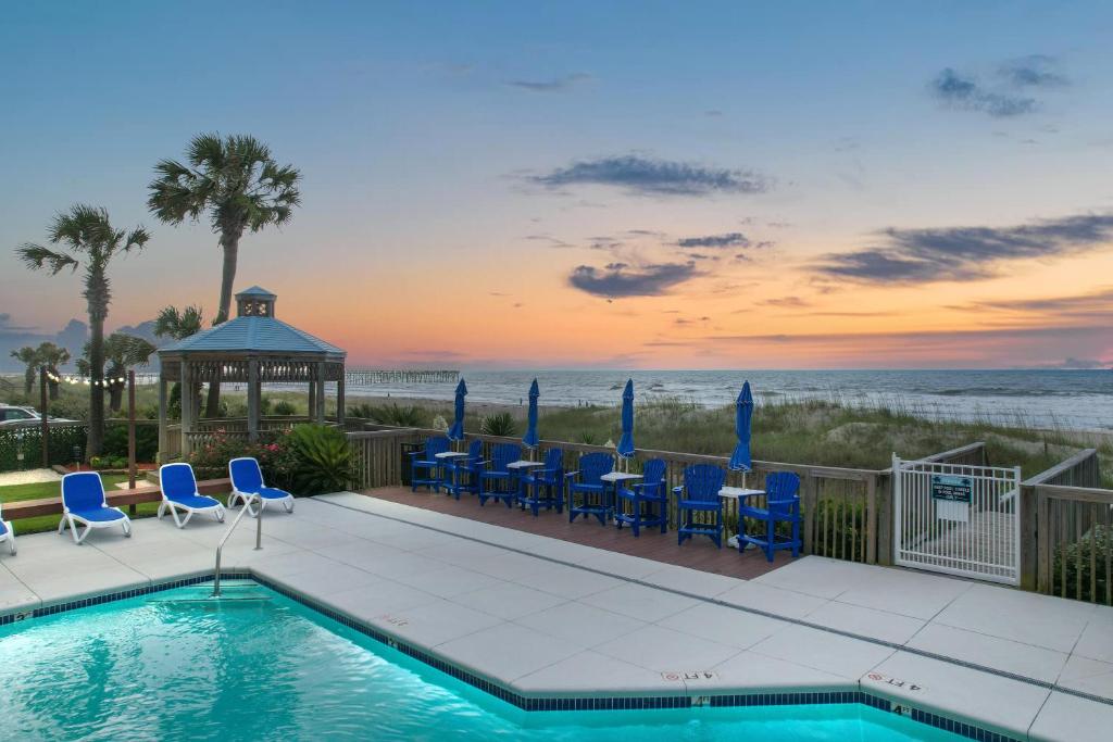 a swimming pool with blue chairs and a gazebo at Ocean Isle Inn in Ocean Isle Beach