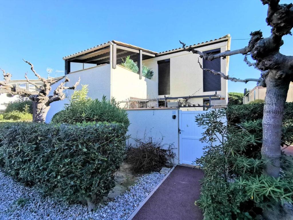 une maison avec une porte blanche et des buissons dans l'établissement Résidence Le Cres De La Ginestelle - Villa 3 pièces - 6 personnes - PORT LEUCATE MAE-5384, à Port-Leucate