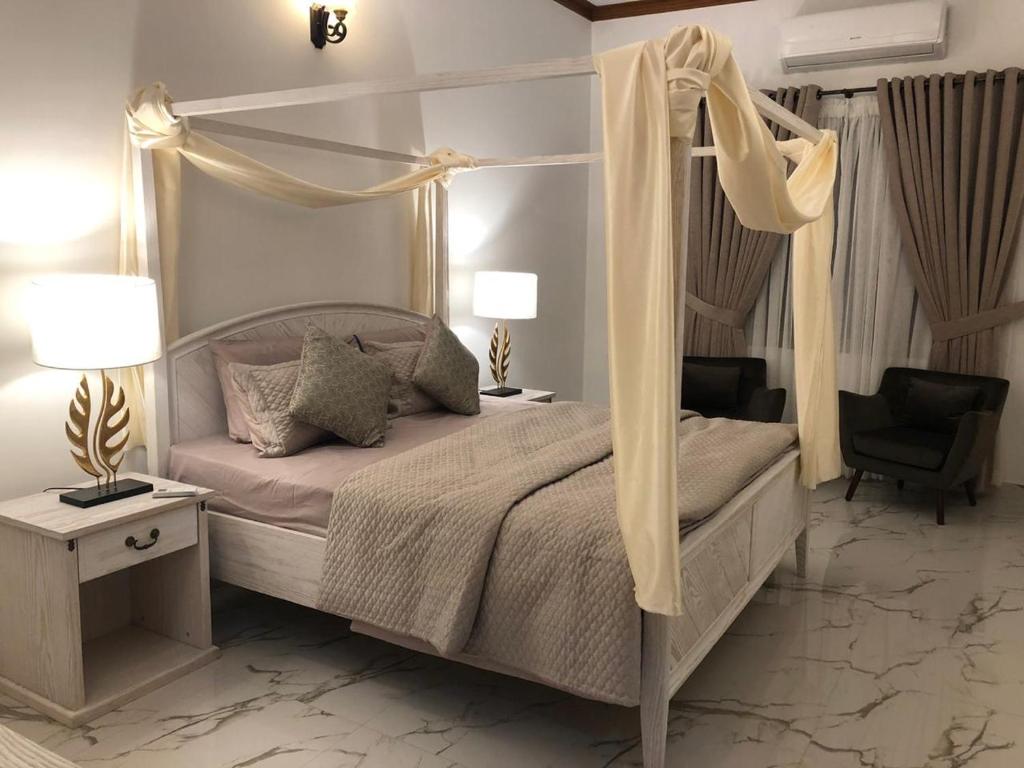 ein weißes Schlafzimmer mit einem Himmelbett und einem Stuhl in der Unterkunft Royal GF Hygiene Gulshan e Iqbal 24 Hrs security auto backup generator in Karatschi