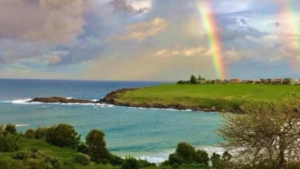 un arco iris sobre un campo verde y el océano en EastsHaven, en Kiama