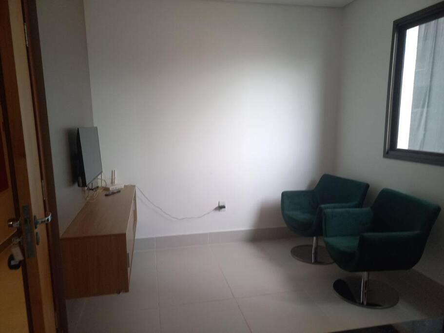 una sala de espera con 2 sillas verdes y TV en Espaço aconchegante com wifi!, en Patos de Minas